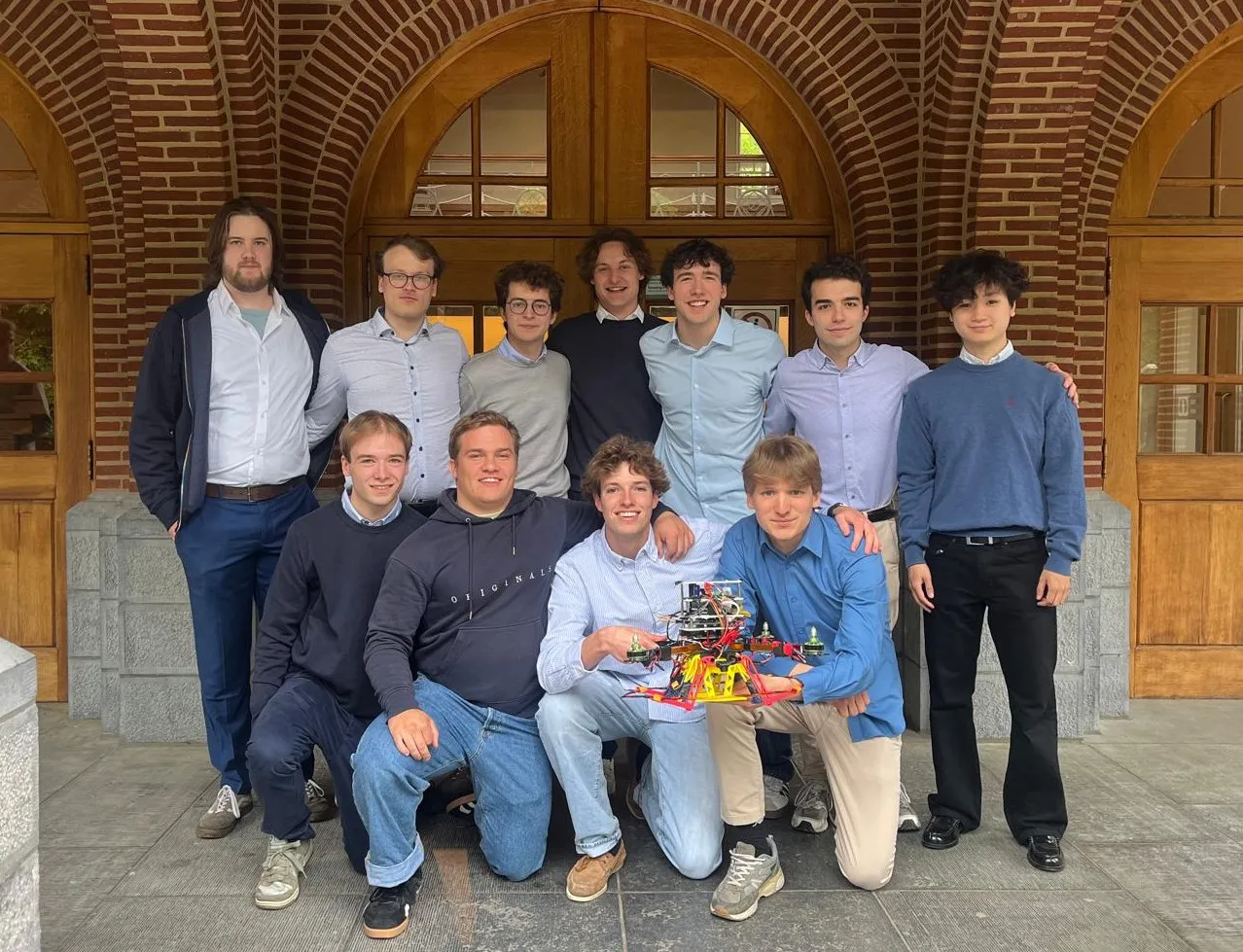 The twelve-person drone team standing in front of a brick archway, holding the finished quadcopter.